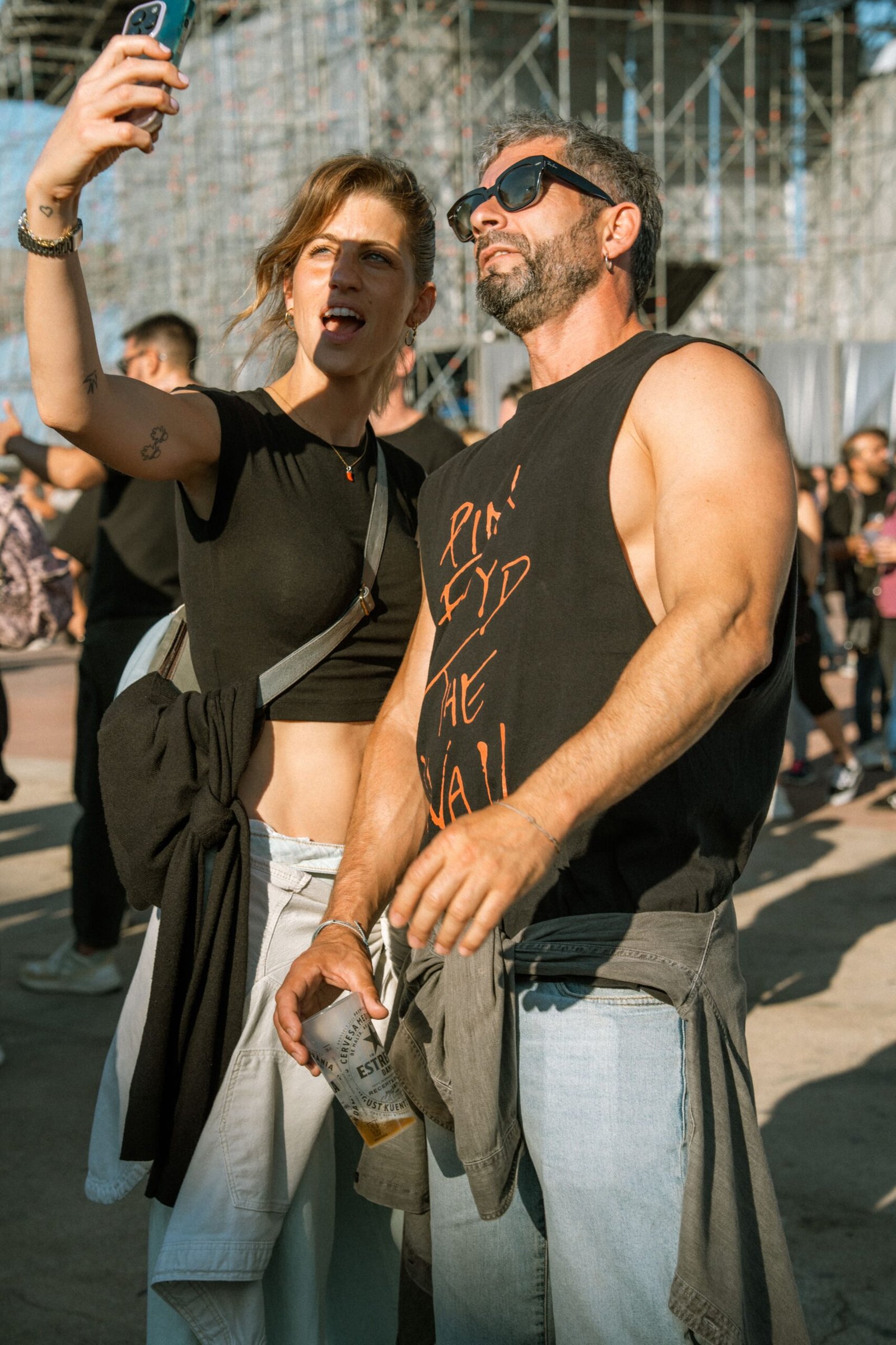 A couple capturing a selfie at an outdoor music festival on a sunny day.