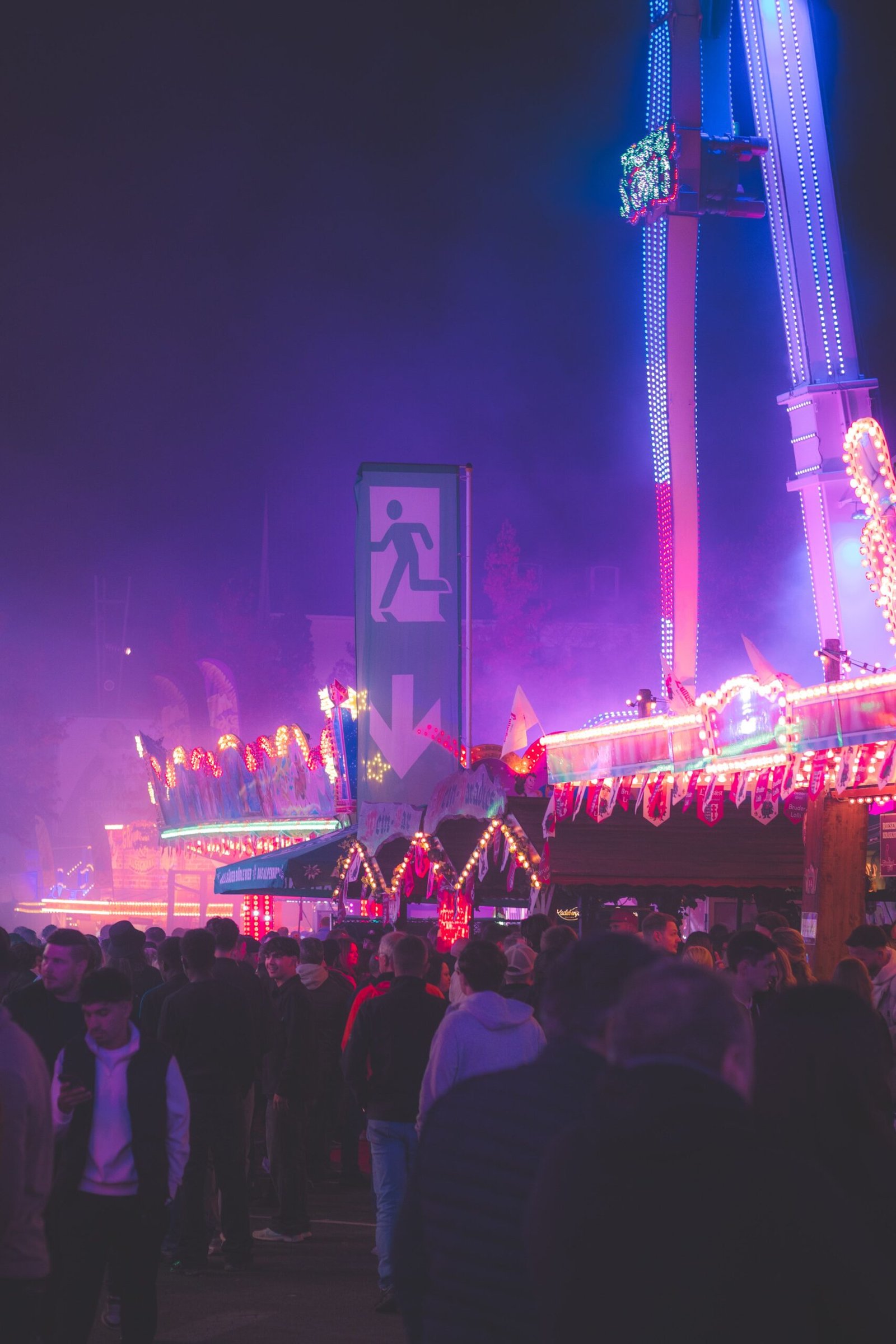 Colorful nighttime scene at a bustling fairground with festive lights and a lively crowd.